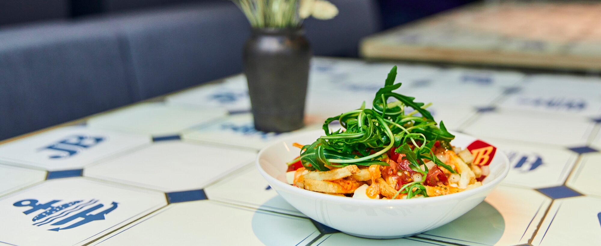 Loaded Fries Italian mit Grana Padano, Tomatensalsa, Rucola und Madurai Sauce in einer weißen Bowl auf JB-Fliesentisch.