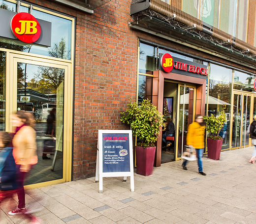 Außenansicht des Jim Block Restaurants in Wandsbek mit Glasfassade, Passanten und Aufsteller am Eingang.