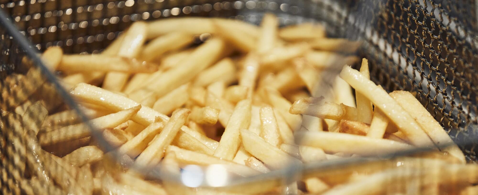 Frisch frittierte Pommes in einem Frittierkorb.