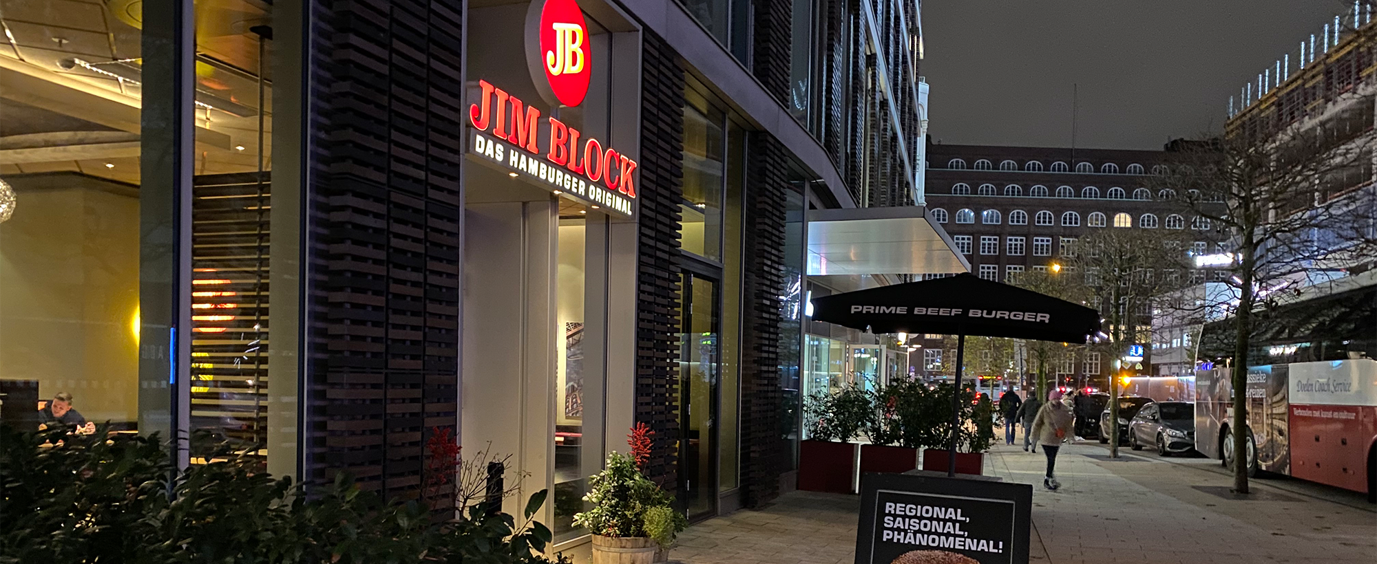 Außenansicht des Jim Block Restaurants am Dammtor bei Nacht, mit leuchtendem Logo und Straßenbeleuchtung.